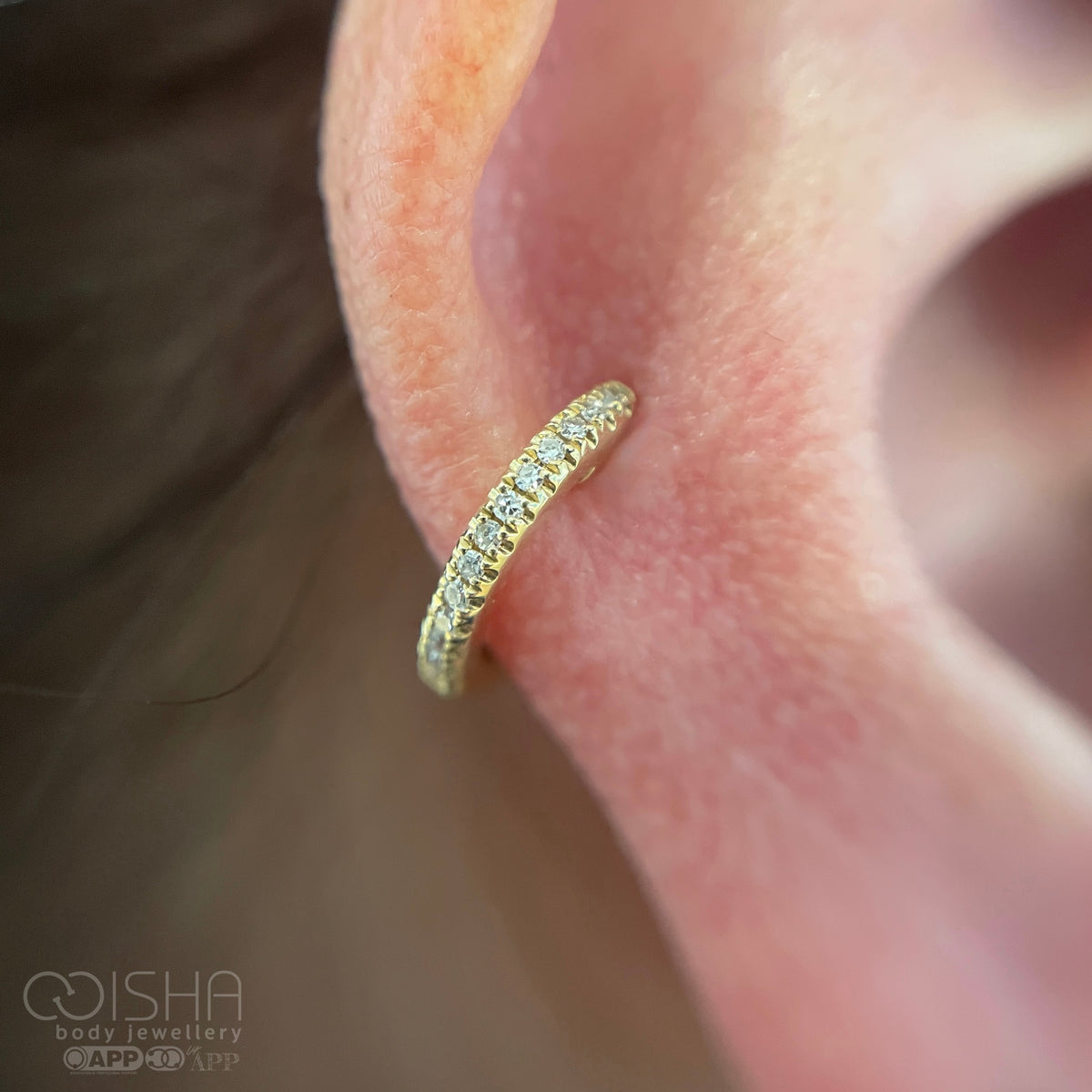 Gold hoop earring worn on a person's ear with 'ISHA body jewellery' branding.