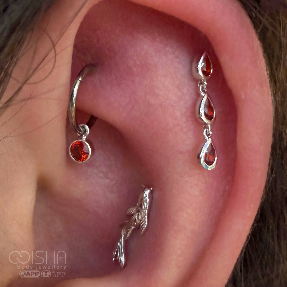 Close-up of an ear with multiple white gold and silver earrings featuring red cz and garnet gemstones. January birthstone