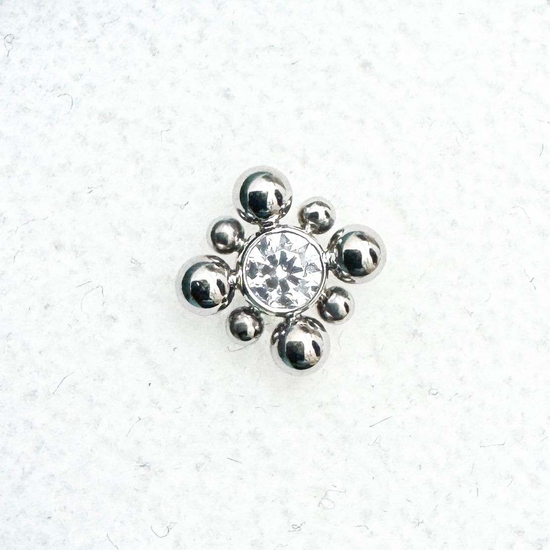 Silver jewelry piece with a central gemstone on a textured white background