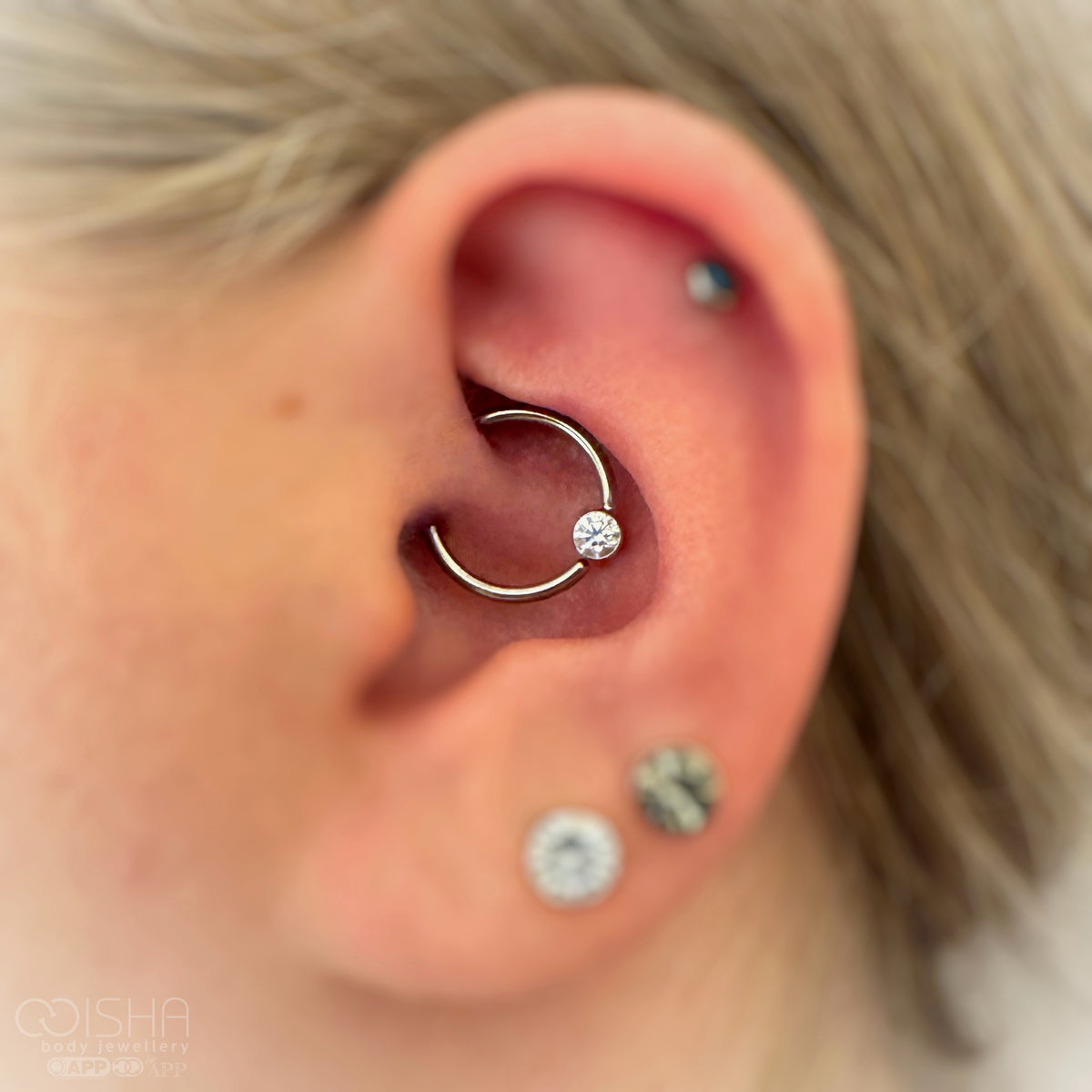 Close-up of an ear with a daith hoop earring and lobe and helix piercings.