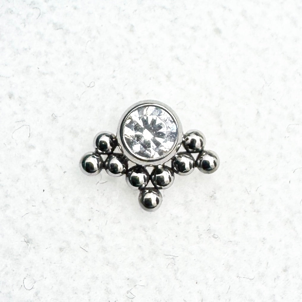 Jewelry charm with a central gemstone surrounded by smaller beads on a textured white background