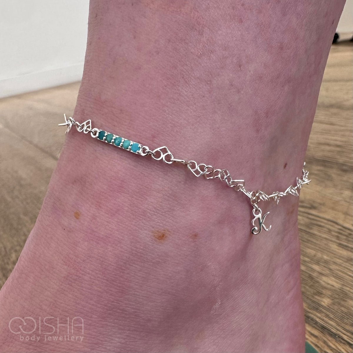 Silver anklet with turquoise stones on a person's ankle, brand 'COISHA' visible.