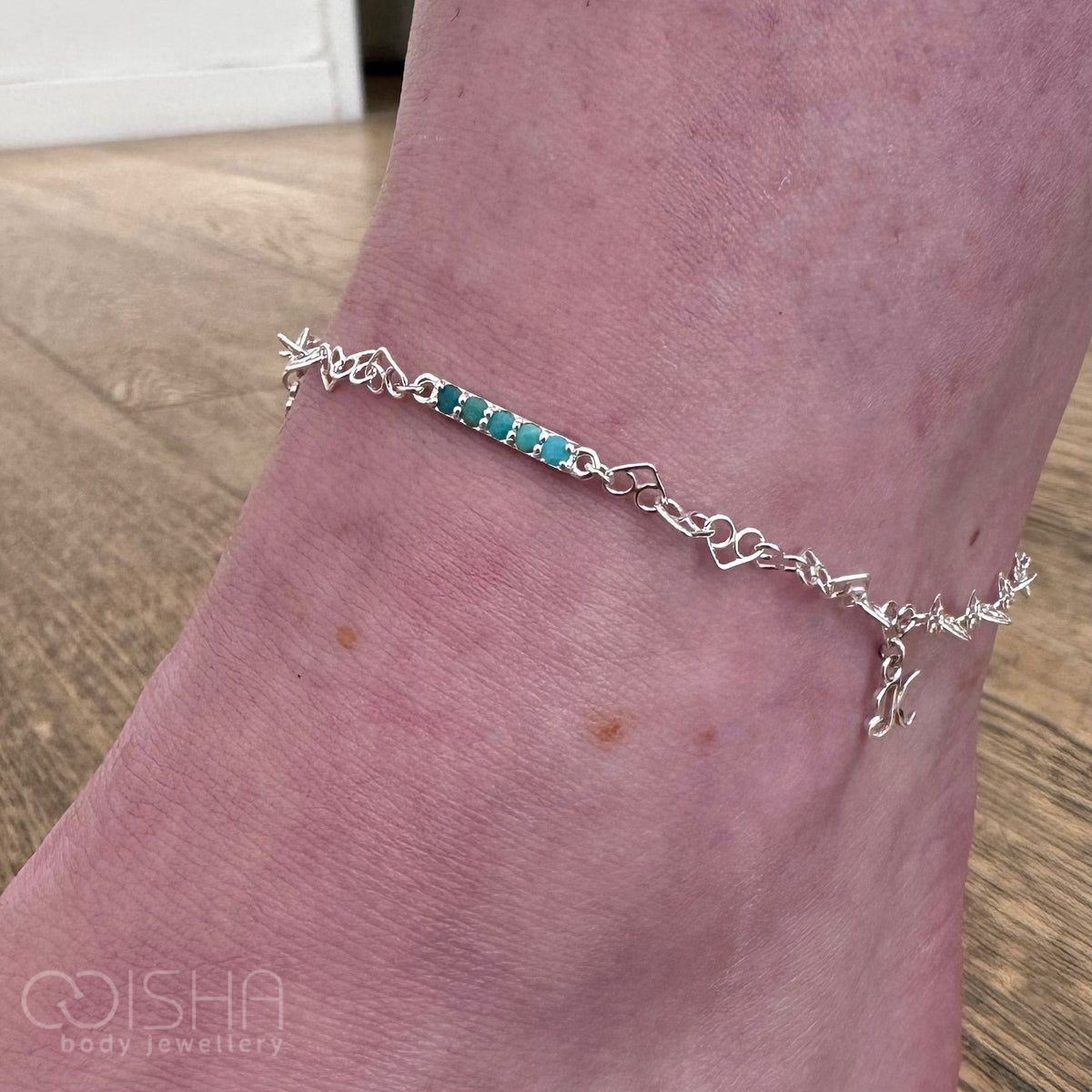 Silver anklet with turquoise beads on a person's ankle against a wooden floor background.