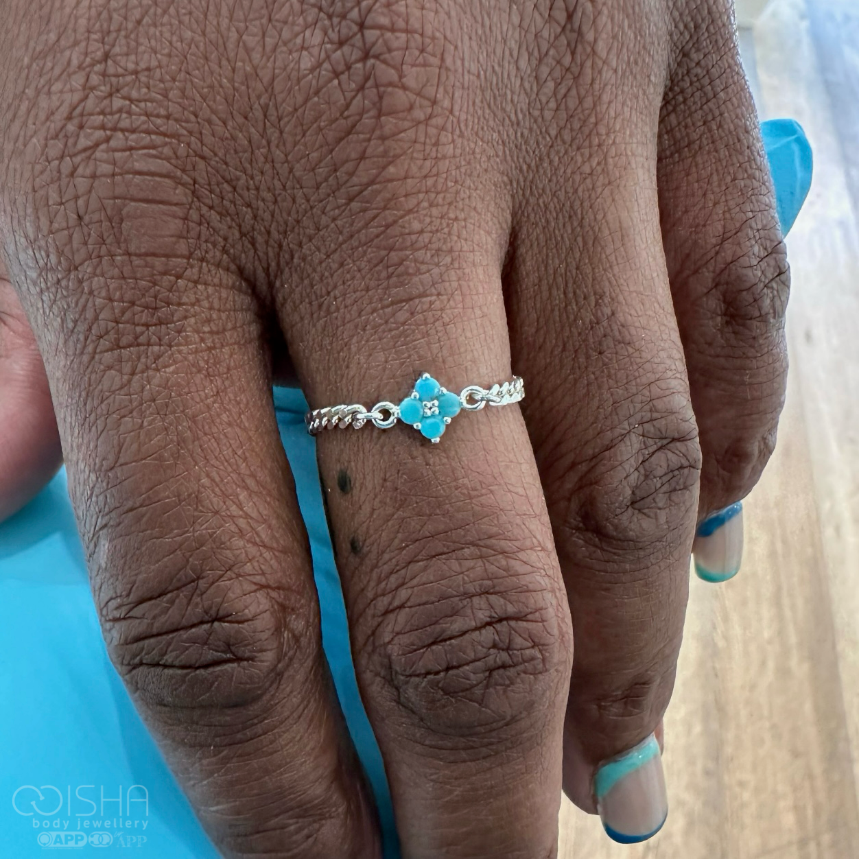 Close-up of a hand wearing a silver ring with a blue gemstone on a blurred background